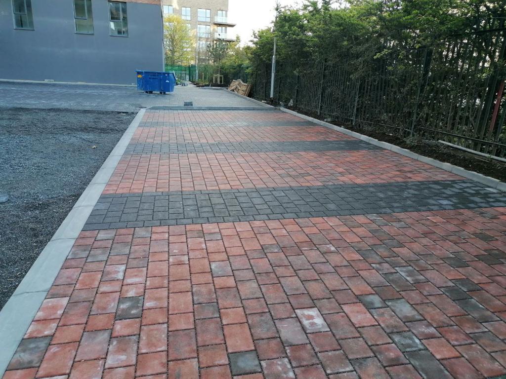 A brick pavement under construction with a small blue skip and a metal fence